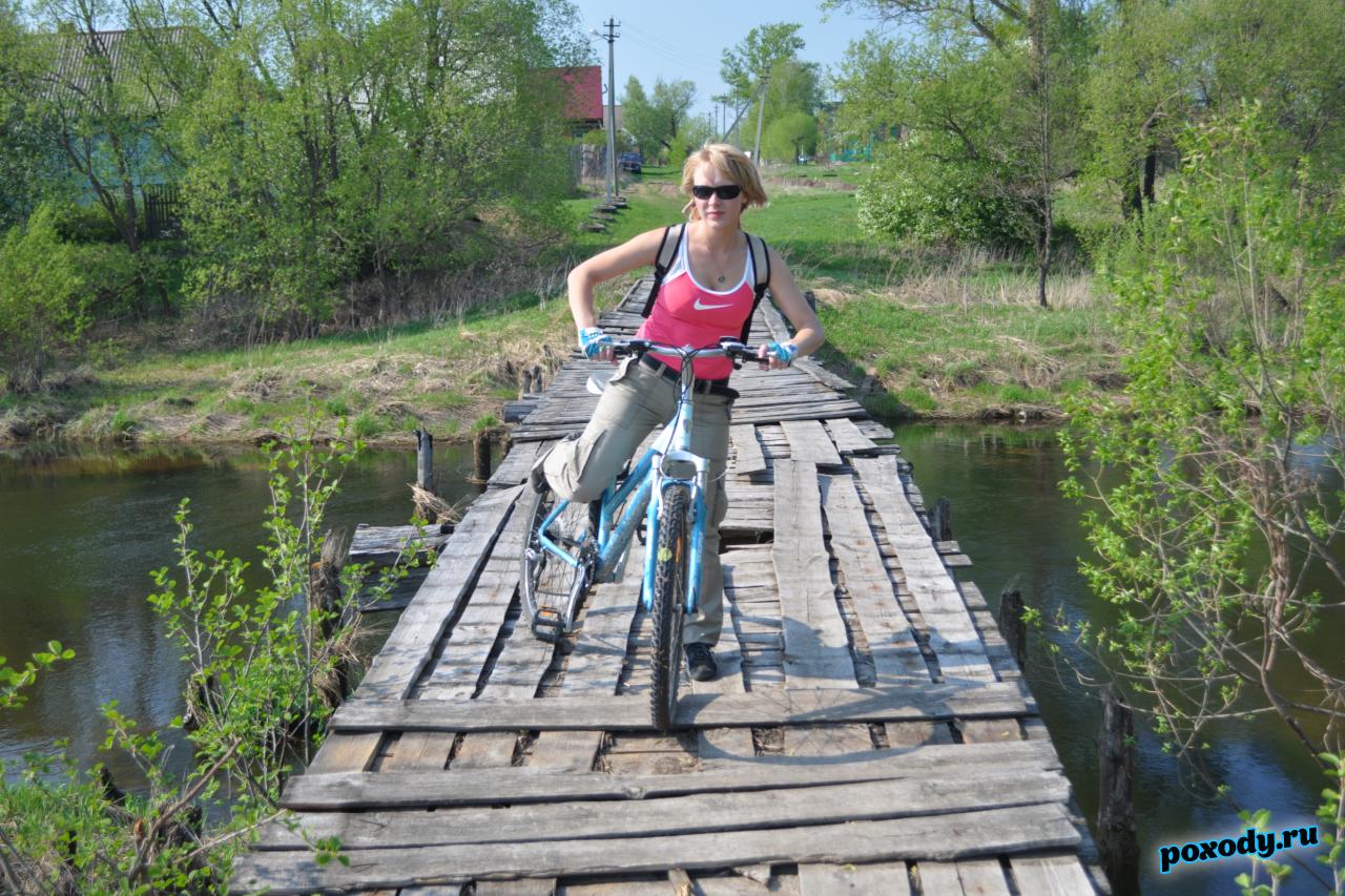 Девушка на велосипеде проезжает по мосту через  реку во время велотура по Владимирской области